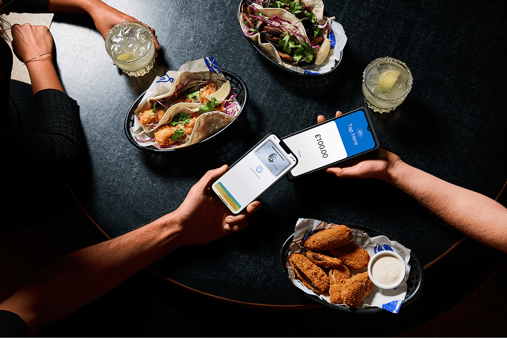 Hands top-view  of a card payment over a table with tacos, salad, fried chicken, and drinks.