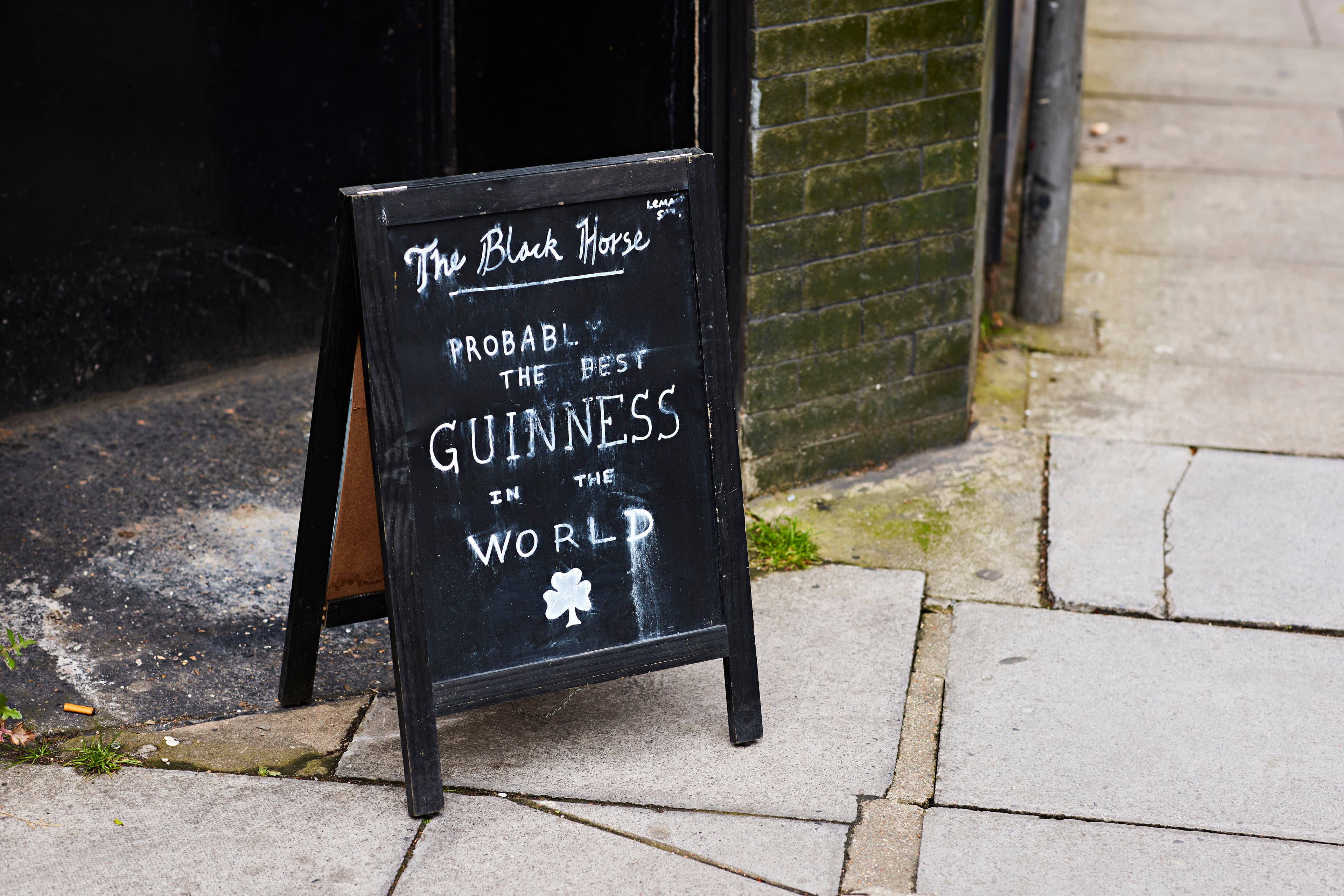 Sidewalk chalkboard sign at "The Black Horse" pub claims "Probably the Best Guinness in the World," with a shamrock illustration.